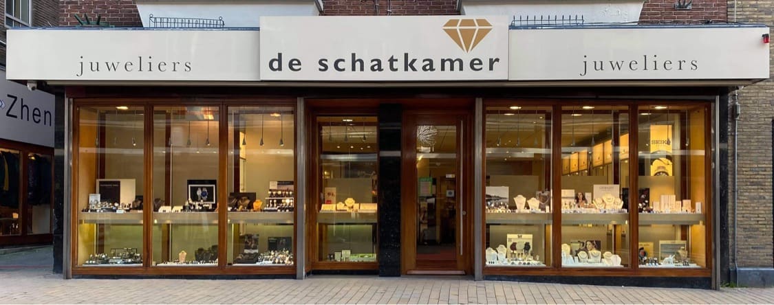 De winkelpui van de Shatkamer Juweliers met verlichte etalages en de naam in gouden letters boven de ingang.