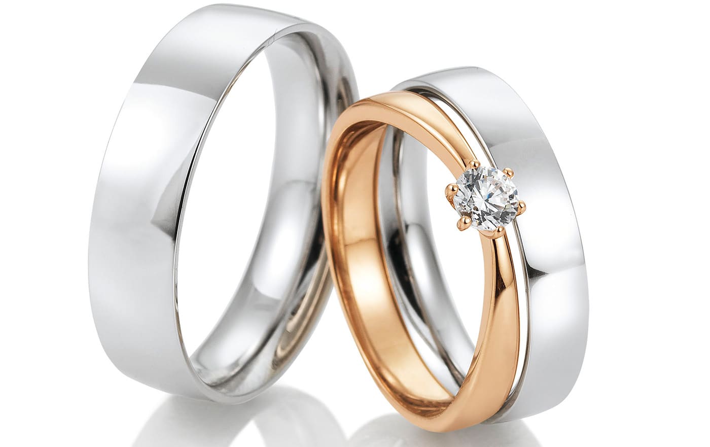 Twee trouwringen naast elkaar, een gladde witgouden ring en een roodgouden ring met een gezette briljant.